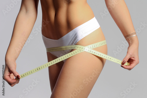 Mid section of woman with sport body measuring her hips with measuring tape 