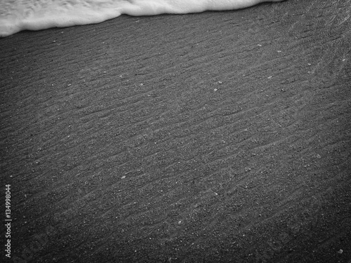 White ocean sea foam and black volcanic sandy surface beach backdrop top view background