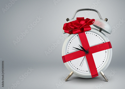 Clock in gift ribbon on grey, time to gift cocept, copy space.
