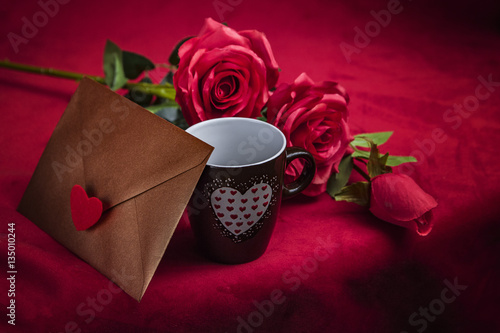 Fototapeta Naklejka Na Ścianę i Meble -  Valentine's Day: Copper gold envelope, cup of coffee and red roses on dark red background
