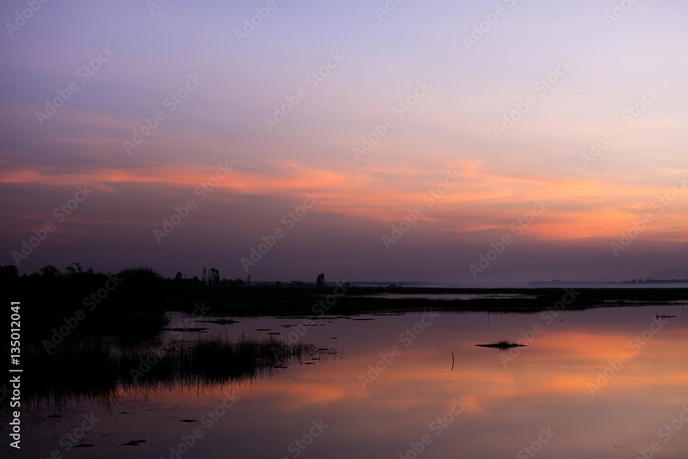 The sky in orange and blue shades is reflected on the water of the river.