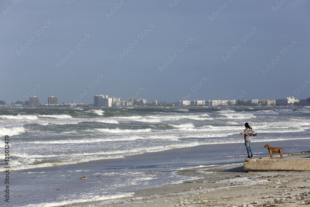 Φωτογραφία A man and his dog stand open arms to the wind blowing off of the Gulf of Mexico on St