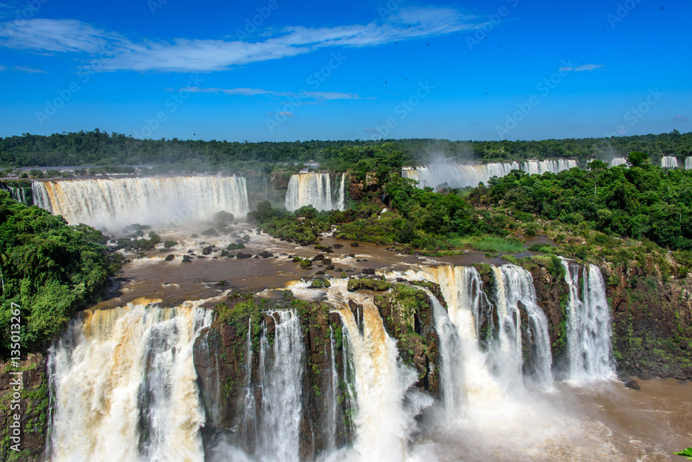 Aerial view of waterfalls cascade of Iguazu Falls with extensive tropical forest and powerful flows of water in Iguacu National Park, UNESCO World Heritage Site, Foz de Iguacu, Parana State, Brazil Aerial view of waterfalls cascade of Iguazu Falls with extensive tropical forest and powerful flows of water in Iguacu National Park, UNESCO World Heritage Site, Foz de Iguacu, Parana State, Brazil