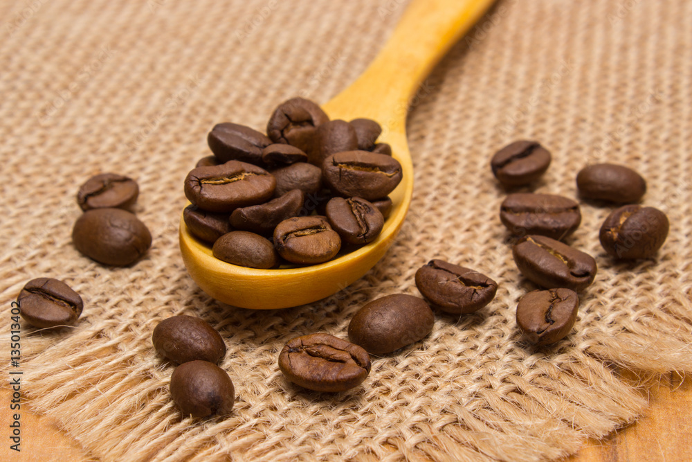 Fototapeta premium Heap of coffee beans with wooden spoon on jute canvas