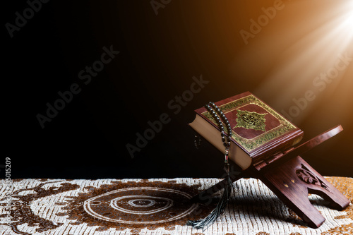 Islam holy book of Muslims, the Quran, is placed on a wooden stand, black background.
