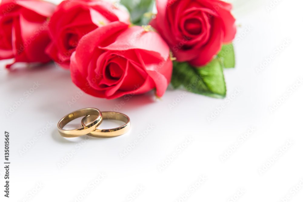 Gold wedding ring placed on a white background. The roses in the background. Gold wedding ring placed on a white background. The roses in the background.