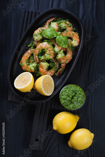 Tiger shrimps with chimichurri sauce on a black wooden surface