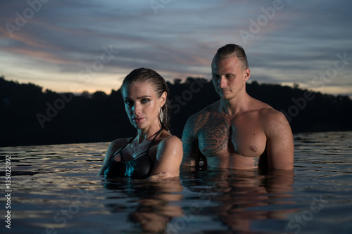Romantic sensual couple alone in infinity swimming pool over beautiful tropical background