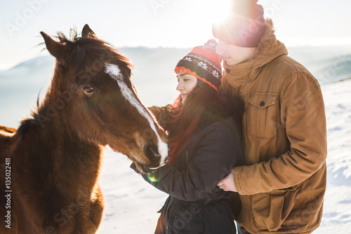 Couple petting and feeding horse with pleasure in shiny sunlight