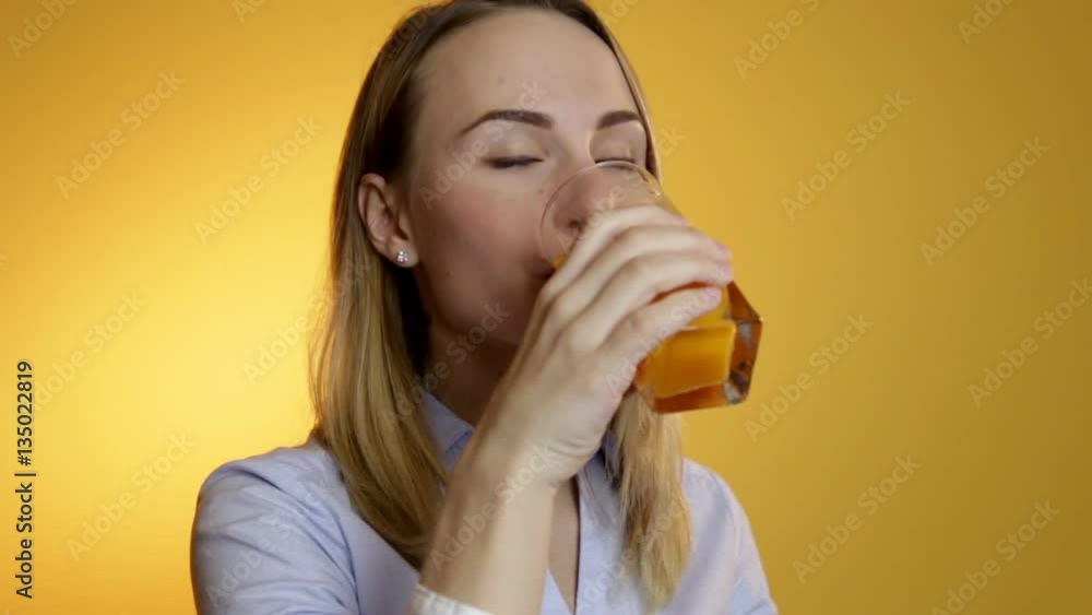 Attractive beautiful young woman drinking juice from a glass on a yellow background Attractive beautiful young woman drinking juice from a glass on a yellow background