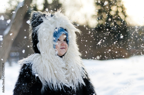 Little girl in fox fur coat looking at the falling snow in winte