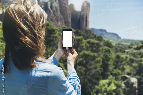 Hipster girl making photo on smartphone mobile closeup, view tourist hands using gadget phone in travel on background mountains landscape; finger touch screen cellphone mockup nature, templates