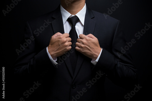 Man in black suit and adjusting his necktie
