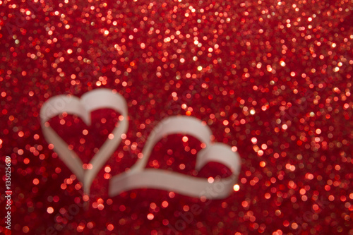 Two white hearts from paper on red shining background blurred