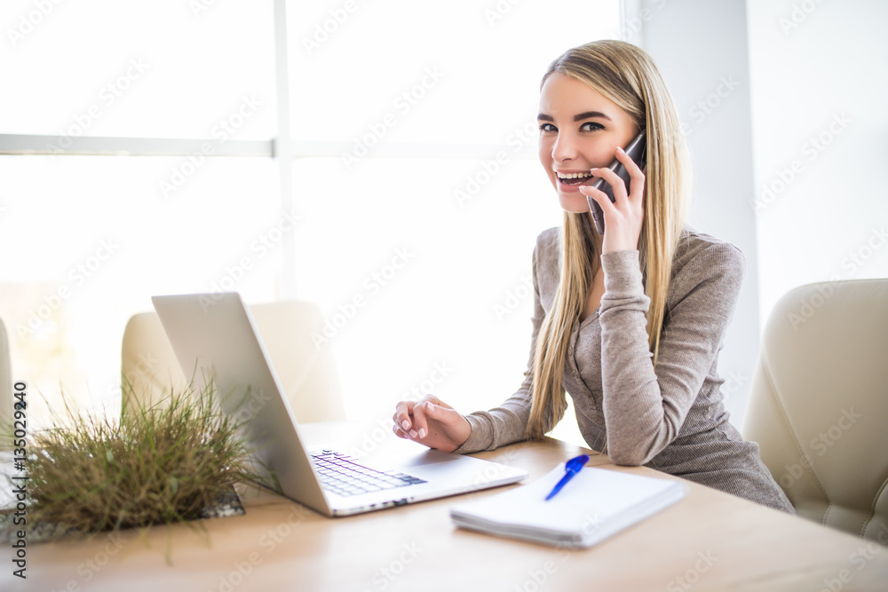 Portrait of a young business woman speak at phone and using laptop at office. Look at camera. Portrait of a young business woman speak at phone and using laptop at office. Look at camera.