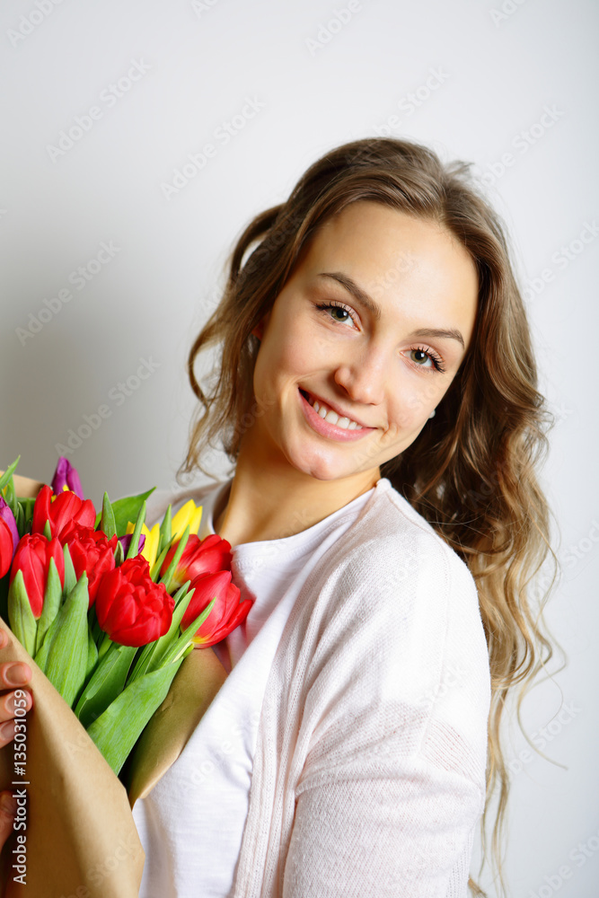 Smiling young woman standing with a bouquet of tulips, looking a Smiling young woman standing with a bouquet of tulips, looking a