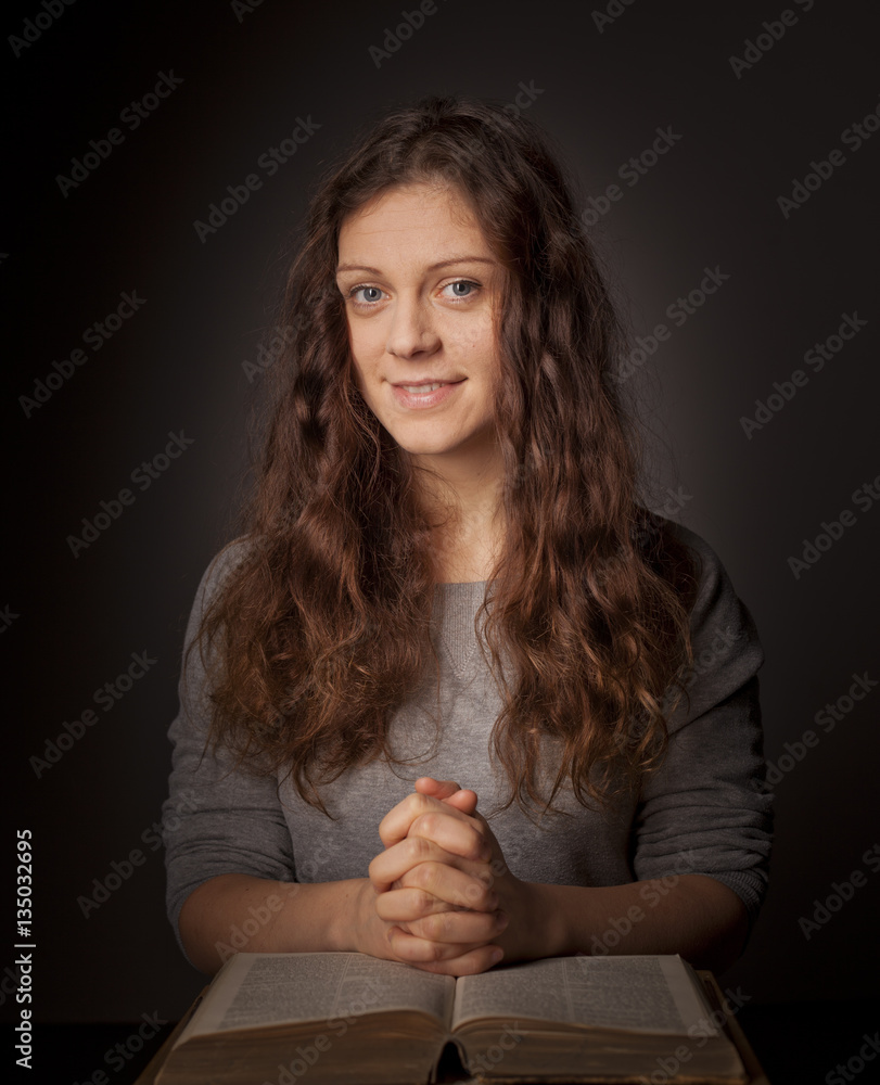 Young woman praying on holy bible with rosary