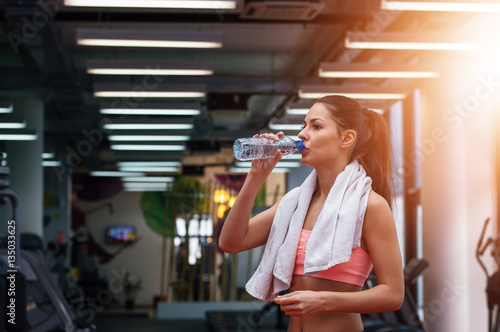 Girl drinking water in gym after workout. Lens flare