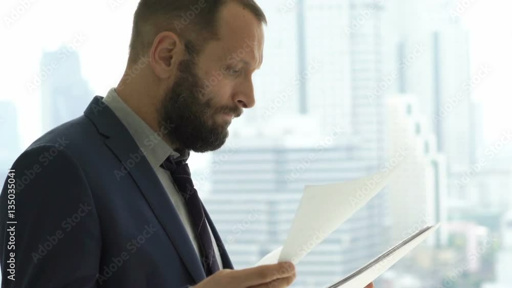 Unhappy, overwhelmed businessman working with documents standing by window at home
Unhappy, overwhelmed businessman working with documents standing by window at home
