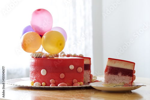 Homemade red birthday cake with air baloons. Slice of a red velv photo