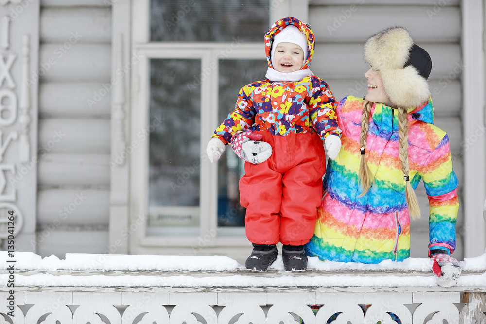 young woman and a young child in a bright colored clothing playing in the winter snow