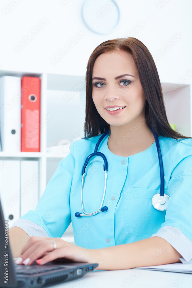 Beautiful female medicine doctor sitting at the table and working at the laptop. Beautiful female medicine doctor sitting at the table and working at the laptop.