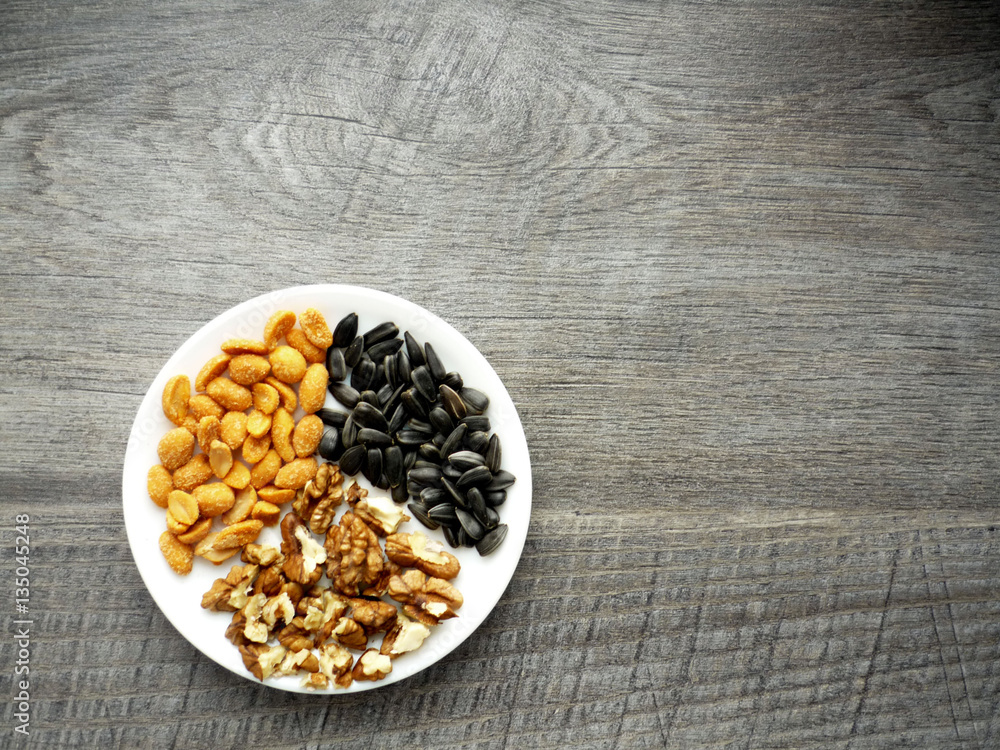 Fototapeta premium nuts ans sunflower seeds on a plate on wooden background