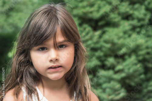 Portrait of attractive angry little girl with long hair outdoors. 