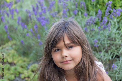 High angle view of cool brunette little girl with violet lavender flower in the background. 