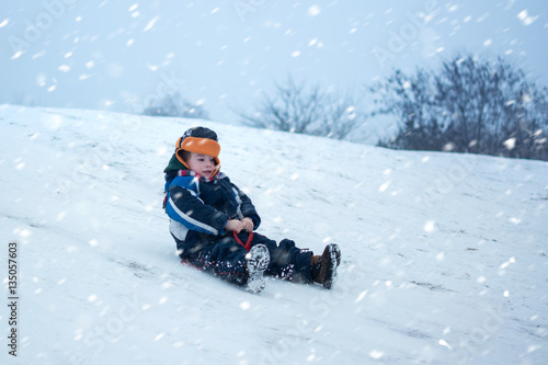Cute little boy with saucer sleds outdoors on winter day. Excited child sledding down a hill.