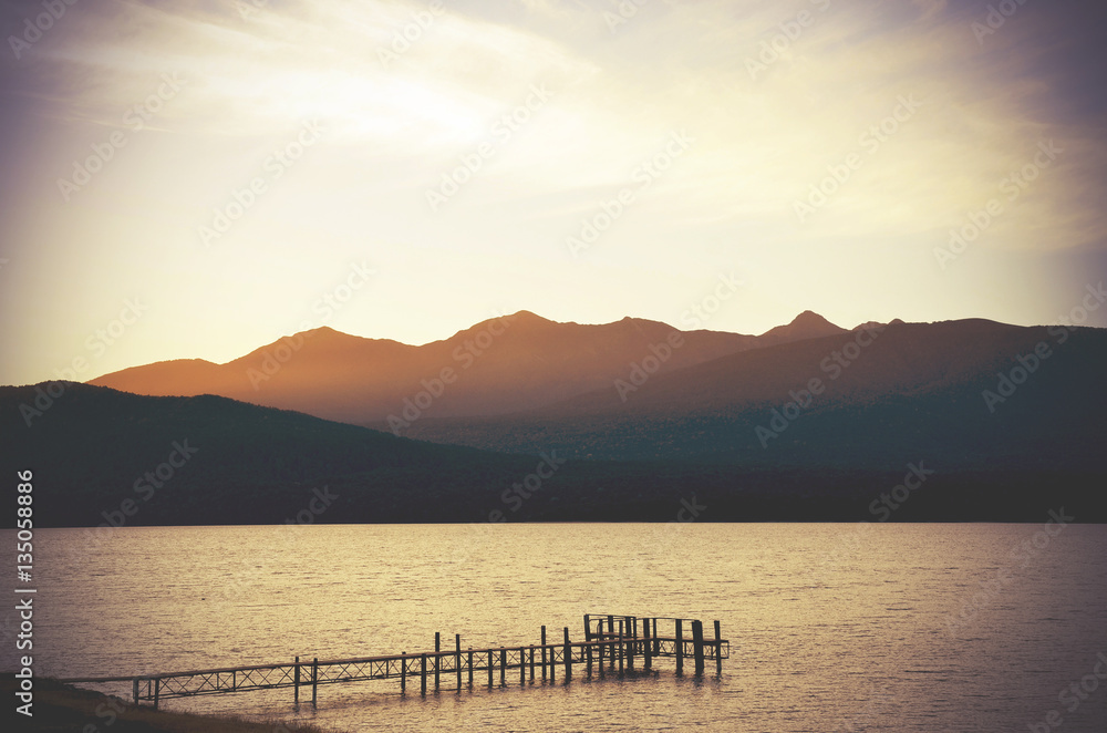 Wispy clouds at dusk over Lake Te Anau jetty, surrounded by mountains and pristine wilderness in fiordland, New Zealand. Retro toned, vignette.