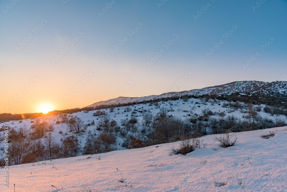 The orange sun sets over the snow-covered mountain. Russia, Stary Krym.
