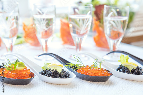 Delicious red and black caviar fish close-up in white and black spoons on white table. Beautifully decorated catering banquet table.