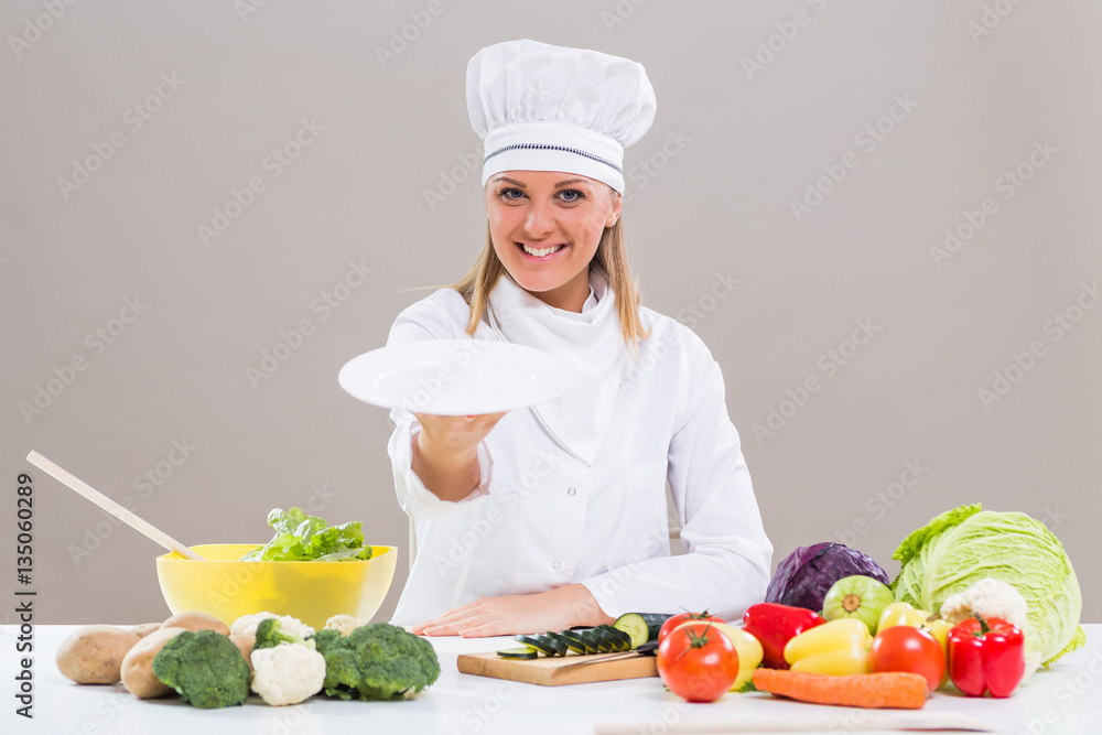 Portrait of cheerful female chef sitting at the table and showing empty plate while making healthy meal.
Portrait of cheerful female chef sitting at the table and showing empty plate while making healthy meal.