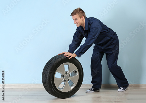 Young mechanic in uniform with wheel, on blue background