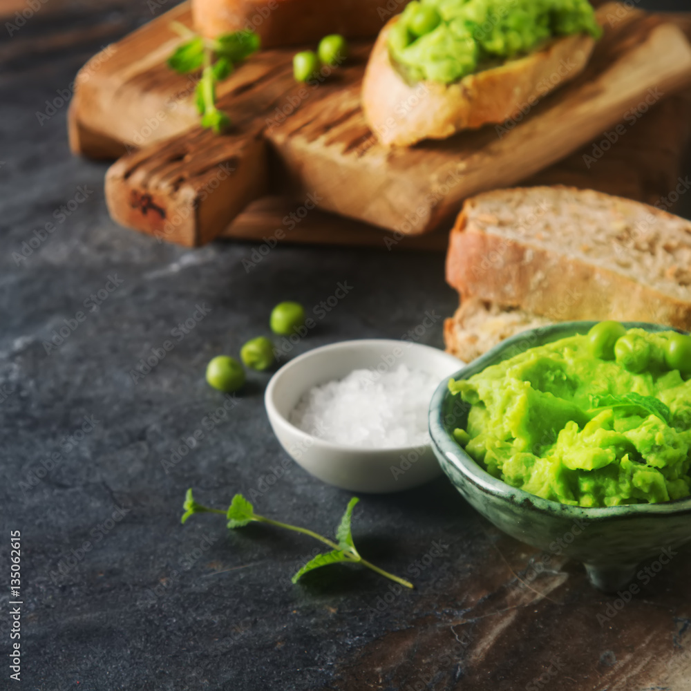 Baguette with mashed green peas and mint. Dark background. Selec