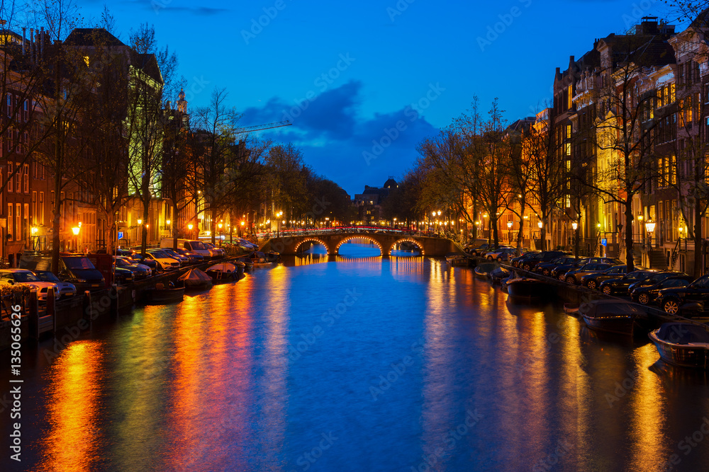 Houses and bridges over canal with lights and reflections at night, Amsterdam, Netherlands