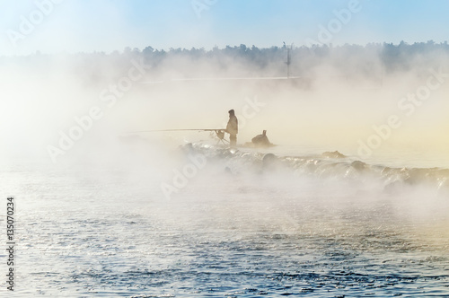 одинокий рыбак на туманном озере с удочкой, ранним утром 