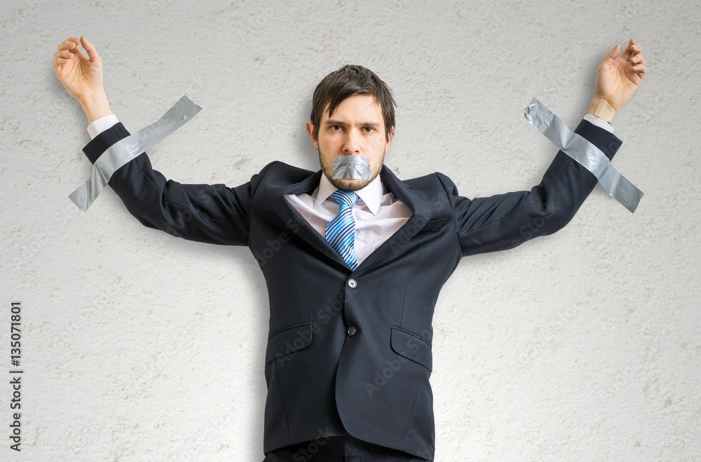 Businessman in suit is taped to the wall with adhesive tape. Businessman in suit is taped to the wall with adhesive tape.