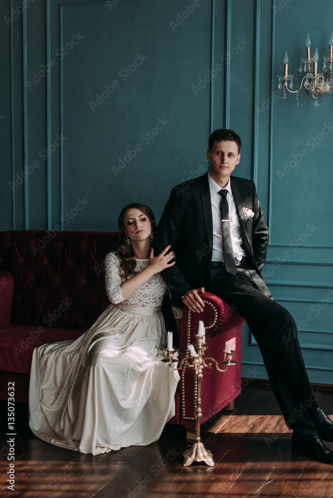 cute wedding couple in the interior of a classic studio posing at the sofa . hey kiss and hug each other, holding hands looking at each other