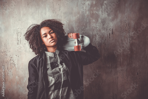 Photography African teenager girl with skateboard in front of a concrete wall