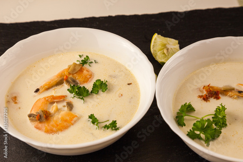 Famous thailand spicy hot soup with red chili peppers, shrimp, lemongrass leaf, ginger root, coconut milk, garlic and parsley. Tom Yum Kung. Asian Dish Cuisine. Black stone on background.