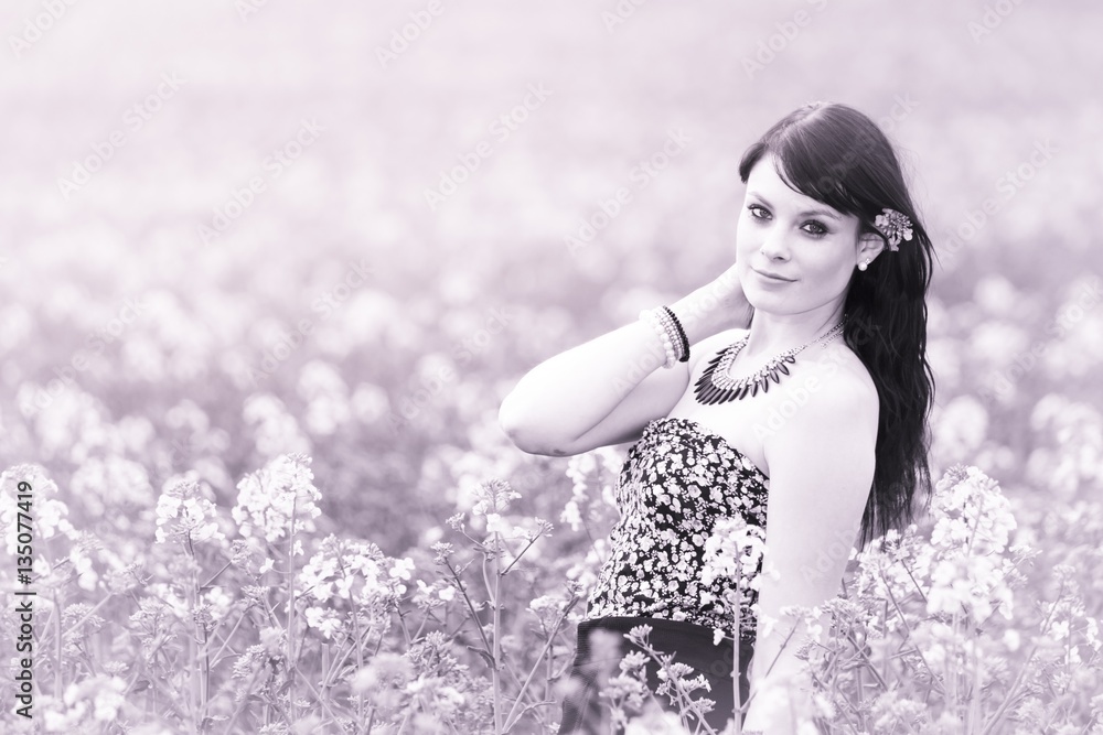 Pretty summer girl posing in pink meadow of flowers. Attractive happy young girl enjoying the warm summer sun and her health in a wide green and yellow meadow. Part of series