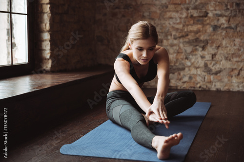 Pretty young fitness woman sitting and stretching her legs