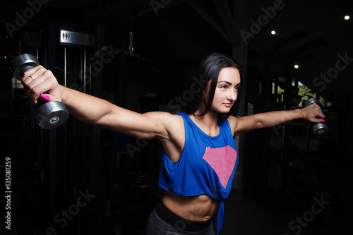 young girl with sexual inflated figure, in the gym, dumbbell lifts pushing hands