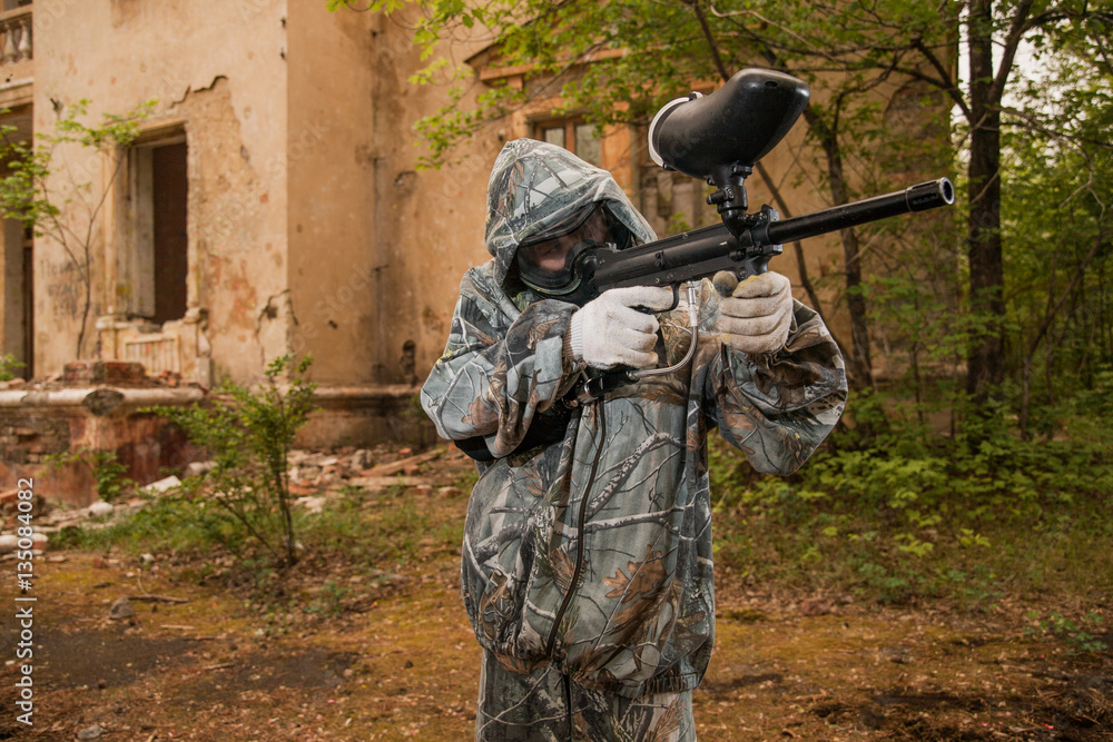 Fototapeta premium young boy playing paintball. boy aiming a paintball gun. Boy in camouflage clothing. boy in a protective suit. Boy in a protective mask. game of war. war game. Boy shoots a gun.