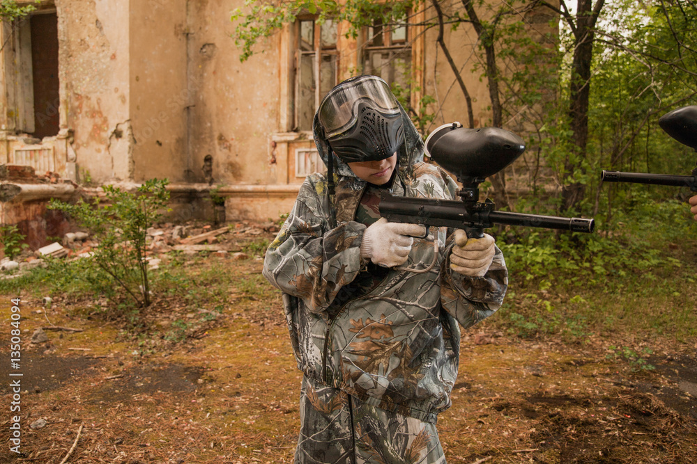 Fototapeta premium young boy playing paintball. boy aiming a paintball gun. Boy in camouflage clothing. boy in a protective suit. Boy in a protective mask. game of war. war game. Boy shoots a gun.