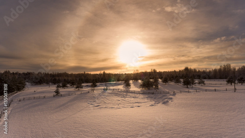 Strong sunset with Halo optical phenomenon.Winter forest in countryside. Aerial view. Russian village
