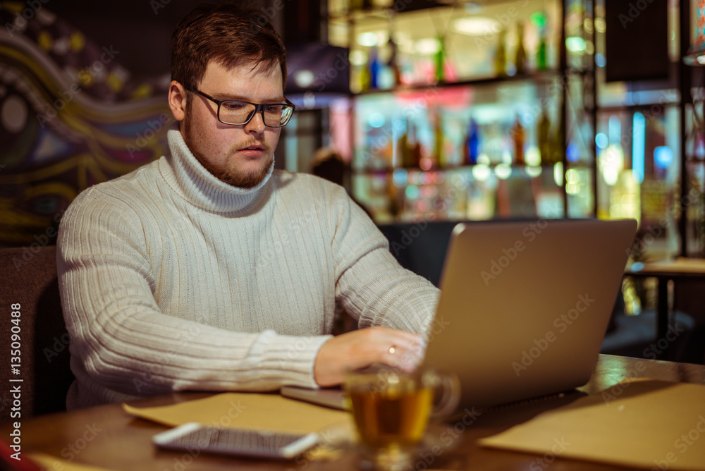 Handsome young man with laptop and cup in a cafe Handsome young man with laptop and cup in a cafe