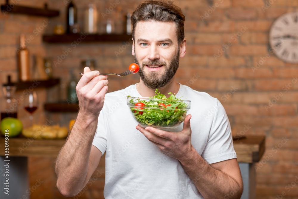 © rh2010 - Handsome bearded man in white t-shirt eating salad with tomatoes in the kitchen. Healthy and vegan food concept © rh2010 - Handsome bearded man in white t-shirt eating salad with tomatoes in the kitchen. Healthy and vegan food concept